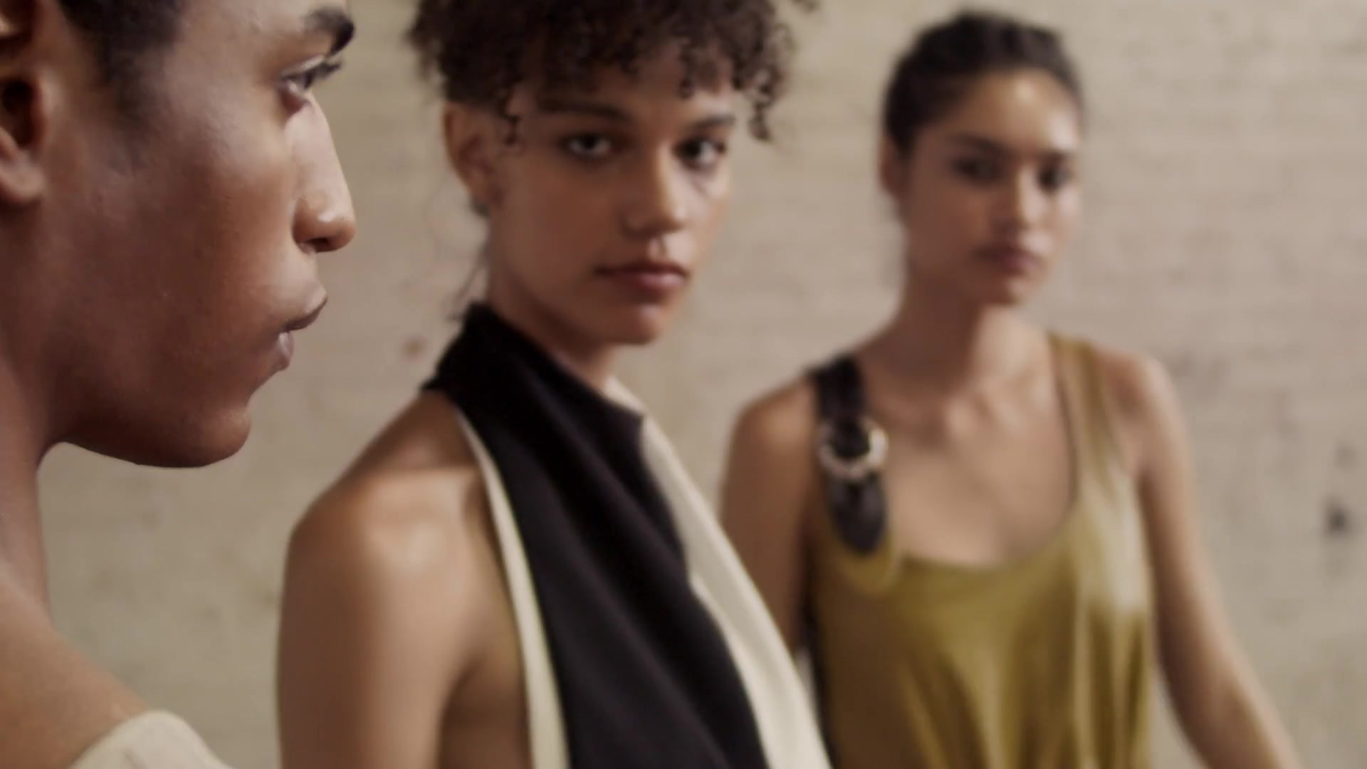 Three people in a close group against a pale textured wall